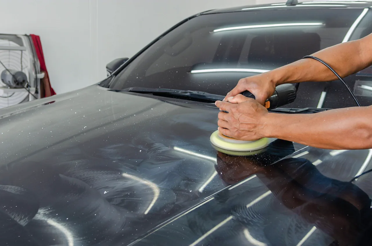 A detailer polishing a black car in a studio